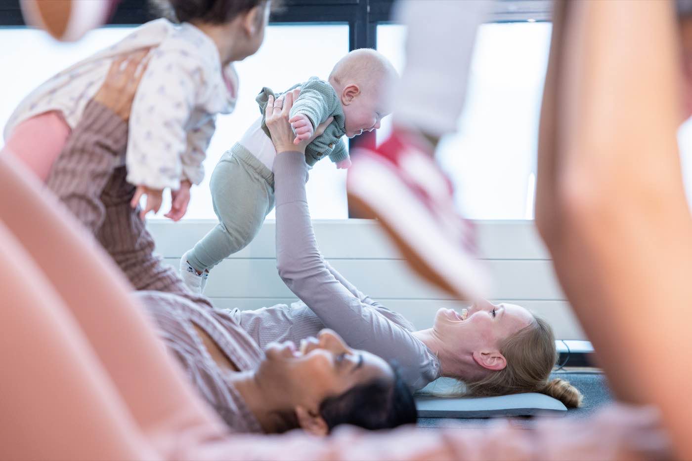 Een moeder tilt haar baby lachend omhoog tijdens Baby Bootcamp